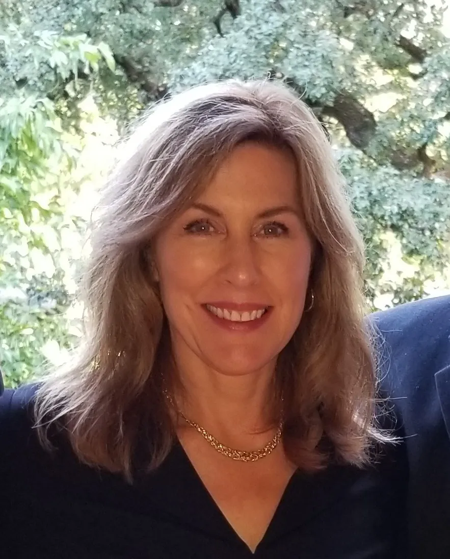 Portrait of Celia O’Connell smiling outdoors in front of leafy green trees